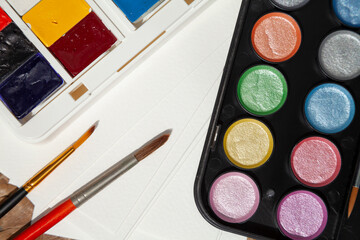 Art supplies close-up: regular and shimmer watercolor paints, brushes, paper. 2 sets of aquarelles prepared for an artist