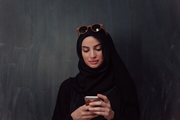 Wall Mural - Young modern muslim business woman using smartphone wearing hijab clothes in front of black chalkboard