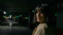 View from behind close up headshot portrait Caucasian woman female lady girl standing at dark empty dangerous parking lot turning back looking at camera with calm face scare afraid in underground