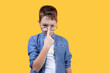 Portrait of a boy on a yellow background. He seriously looks at the camera and adjusts his glasses with his finger. Front view