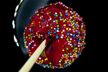Apple On A Stick In Red Caramel With Multi-colored Icing On A Black Background