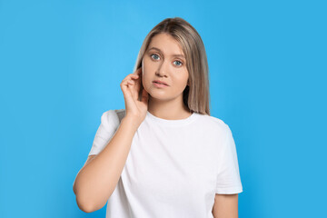 Wall Mural - Young woman suffering from ear pain on light blue background