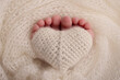 The tiny foot of a newborn baby. Soft feet of a new born in a wool white blanket. Closeup of toes, heels and feet of a newborn. Knitted heart in the legs of baby. Macro studio photography. 