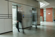 © pressmaster - Part of spacious corridor inside modern office center and two blurred businessmen by elevators with glass doors moving along