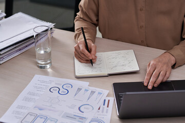 Poster - Close-up of hands of female entrepreneur analyzing graphic data and making notes in notebook while working over new project