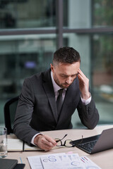 Poster - Overworked chief executive office with hand on temple feeling sick while sitting in front of laptop by workplace and analyzing online data