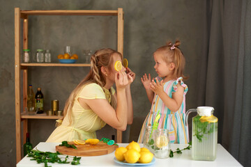 mother jokes and fooling around with daughter in kitchen at home. family makes vitamin lemonade toge