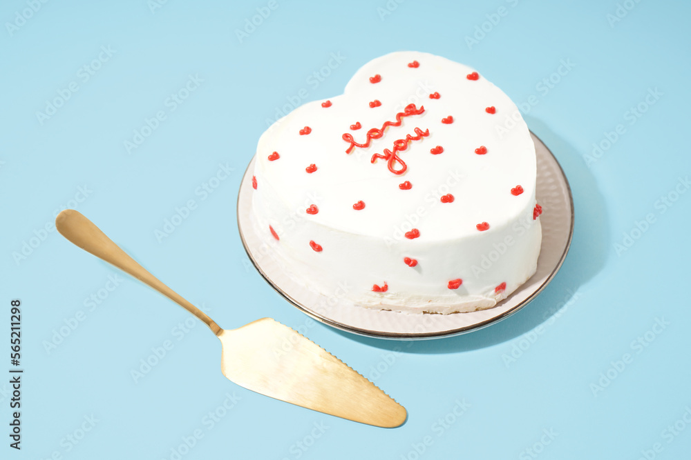 Plate with heart-shaped bento cake, and spatula on blue background. Valentine's Day celebration