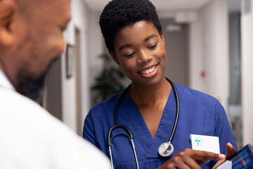 Wall Mural - Smiling african american male and female doctor using tablet in hospital corridor