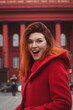 © Gypsy On The Road - Close up excited woman wearing red coat on street portrait picture. Closeup side view photography with city building on background. High quality photo for ads, travel blog, magazine, article