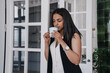 © Iona - Serious tAfrican american young woman having break holding cup of coffee smiling leaning on door at office. Cheerful Brazilian businesswoman relaxing at home, business and education.