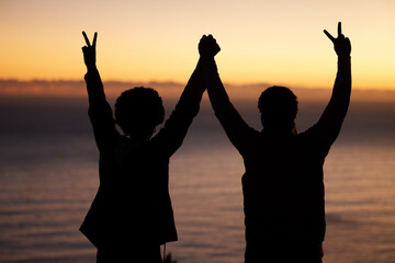 Canvas Print - Sunset, beach and silhouette of couple celebration, success or winning and holding hands in shadow, night or dark. Sky, ocean and winner people in rear with peace sign for sea, hiking or travel goals