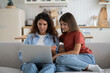 © DimaBerlin - Young woman mother and adolescent girl daughter using laptop, talking to family via computer, sit on couch at home, mom and child look at pc screen have online video call with father, selective focus