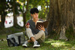 © Prathankarnpap - Peaceful asian man reading book on green grass with sunlight from a sunset shining through tree branch