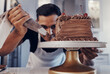 © Coetzee/peopleimages.com - Piping, chef and man baker baking a cake with chocolate in a kitchen or pastry cook preparing a sweet recipe. Food, dessert and cook preparing a sweet meal in Brazil and adds cream or icing