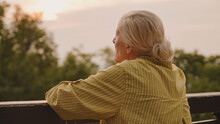 Pensive Senior Woman Standing Near Fence Alone, Looking At Sunset, Life Memories