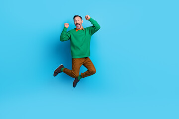 Poster - Full body photo of mature handsome man jumping high energetic raise fists dressed stylish green outfit isolated on blue color background