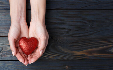 Female hands holding red love heart on wooden background, view from above