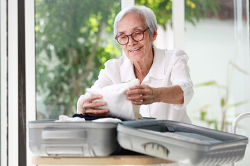 Excited asian senior woman folding clothes into suitcase,Healthy old elderly packing luggage for trip,summer vacation travel and happy life after retirement,take care of your health,healthcare concept