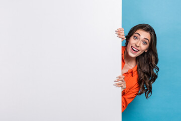 Poster - Photo portrait of young pretty girl hiding behind white wall excited dressed stylish orange outfit isolated on blue color background