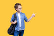 Portrait of a boy with a backpack on a yellow background. He looks right and points at something there with his finger. Front view. Copy space. Suitable for collage and banner making and other design