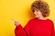 Horizontal shot of happy woman poses against yellow background points away on free space for your advertising content