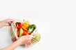Women's hands take out fresh vegetables from a bag on a white table. Top view, flat lay