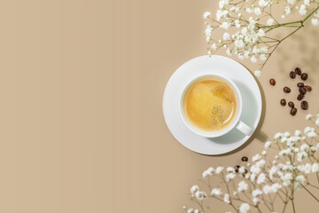 coffee composition with cup of natural coffee and coffee beans on beige background with white flower