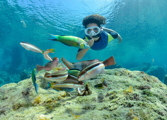 Young boy snorkeling underwater with a small colorful fish,