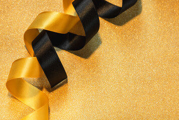 Black and gold satin ribbon on sparkling gold wrapping paper. Festive gift wrapping.