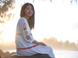 © Austockphoto - Smiling Chinese woman sitting on rocks by the shore in the evening