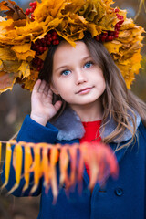 Close-up portrait of a little girl with blue eyes and a wreath of maple