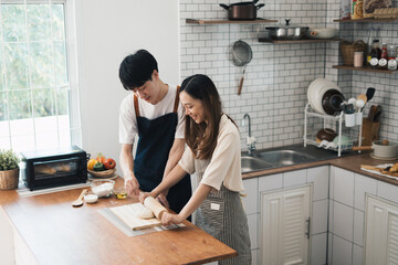 Asian couple standing in kitchen at home preparing together yummy dinner on first dating, spouses chatting enjoy warm conversation and cooking.