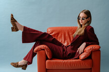 Fashionable Confident Woman Wearing Elegant Marsala Color Suit, Sunglasses, Leopard Print Loafer Shoes, Posing, Sitting In Brown Leather Armchair. Studio Fashion Portrait. Copy. Empty Space For Text