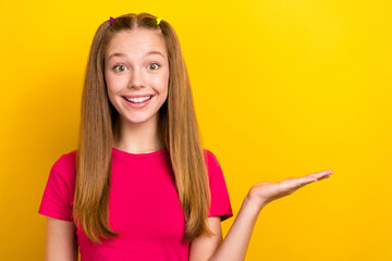 Sticker - Closeup photo of excited funky teenager woman wearing pink t-shirt hold arm empty space advert new product brand isolated on yellow color background