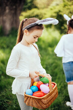 Easter Egg Hunt. Girl Child Wearing Bunny Ears Running To Pick Up Egg In Garden. Easter Tradition. Baby With Basket Full Of Colorful Eggs. Bunny In Basket