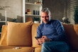 © Zamrznuti tonovi - Middle aged man using smartphone while sitting on a sofa at home