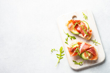 Sticker - Open sandwiches with cream cheese, prosciutto and arugula at white background. Top view with copy space.