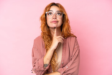 Wall Mural - young caucasian woman isolated on pink background with glasses and looking up