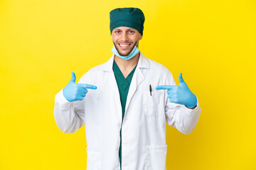 Wall Mural - Surgeon blonde man in green uniform isolated on yellow background proud and self-satisfied