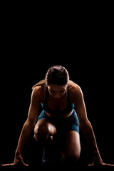 Wall Mural - Female runner in low race start position. Girl in sportswear against dark background..