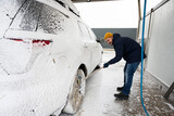 Fototapeta  - Man washing american SUV car with mop at a self service wash in cold weather.