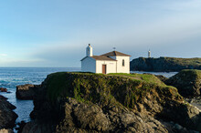 Hermitage On Some Cliffs On The Galician Coast, Over The Atlantic Ocean With A Blue Sky And The Frouxeira Lighthouse In The Background.