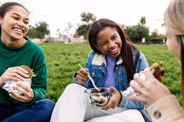 Group of university female students sit on grass outdoor on campus college while having lunch