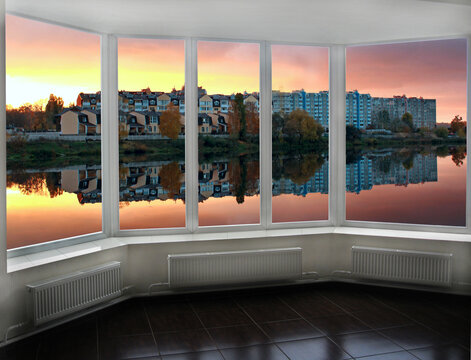 Panoramic window with view of red sunset above city buildings. Evening cityscape