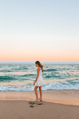 Poster - Adorable teen girl in white on the seashore during her beach summer vacation with amazing sky on background