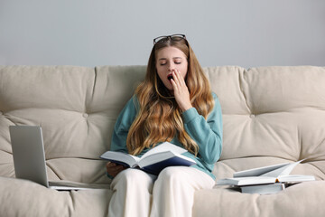 Wall Mural - Young tired woman studying on couch indoors