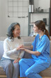 © NanSan - Portrait of attractive young caucasian female nurse elderly caregivers with senior patient home caring for elderly asia female patients on couch, indoors. hand clasp to encourage
