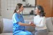 © NanSan - Portrait of attractive young caucasian female nurse elderly caregivers with senior patient home caring for elderly asia female patients on couch, indoors. hand clasp to encourage