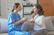 © NanSan - Portrait of attractive young caucasian female nurse elderly caregivers with senior patient home caring for elderly asia female patients on couch, indoors.